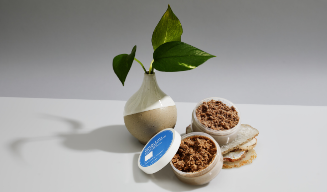 A selection of LATHER body scrubs in front of a neutral colored vase