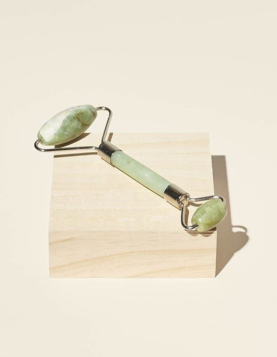 Jade roller tool perched on a block on light birch wood.