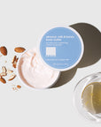 jar of body butter opened pictured next to almonds and bowl of oil