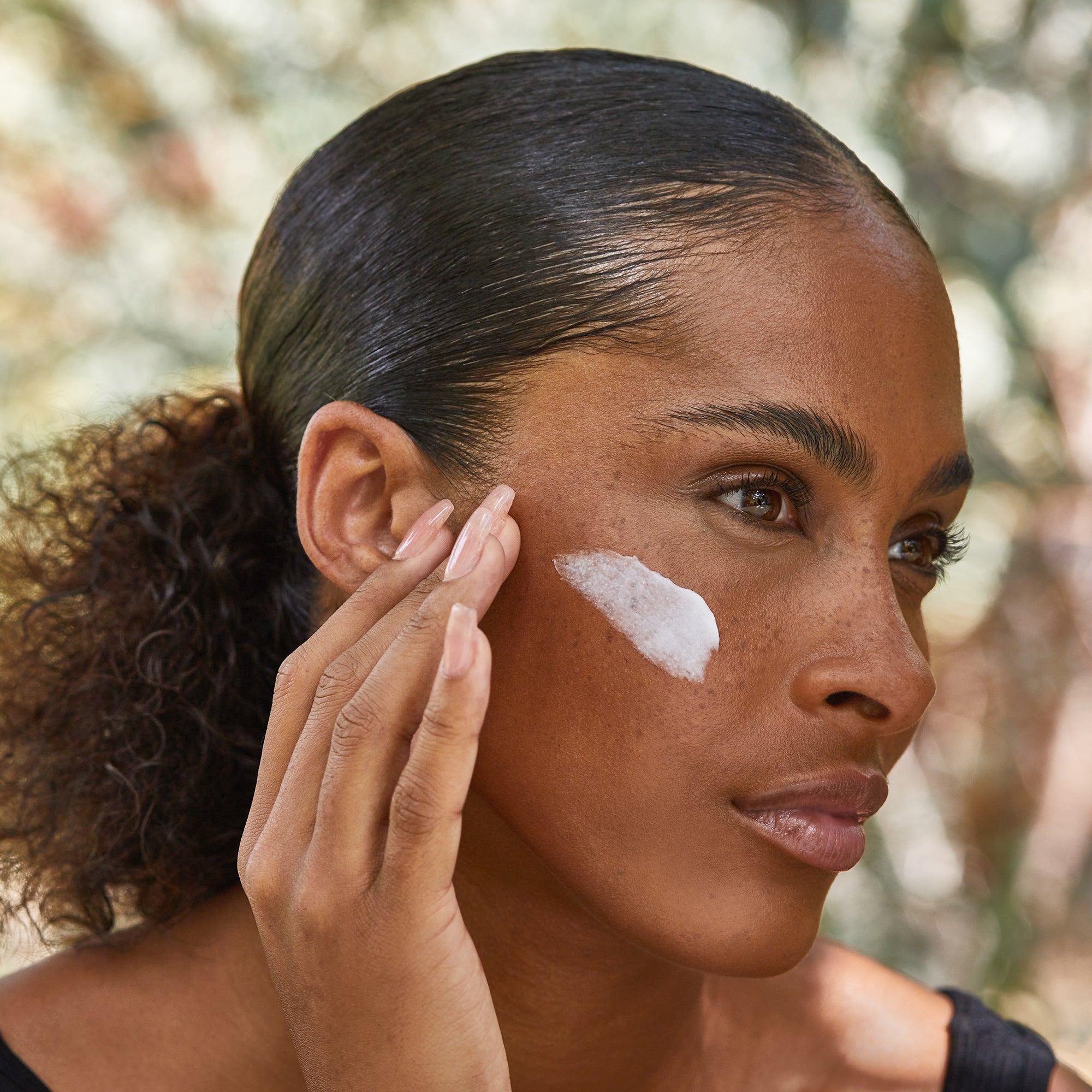 Woman applying moisturizer to her cheek.