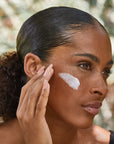 Woman applying moisturizer to her cheek.