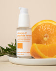 Skincare bottle placed on plate with orange and rosemary placed adjacent to it.