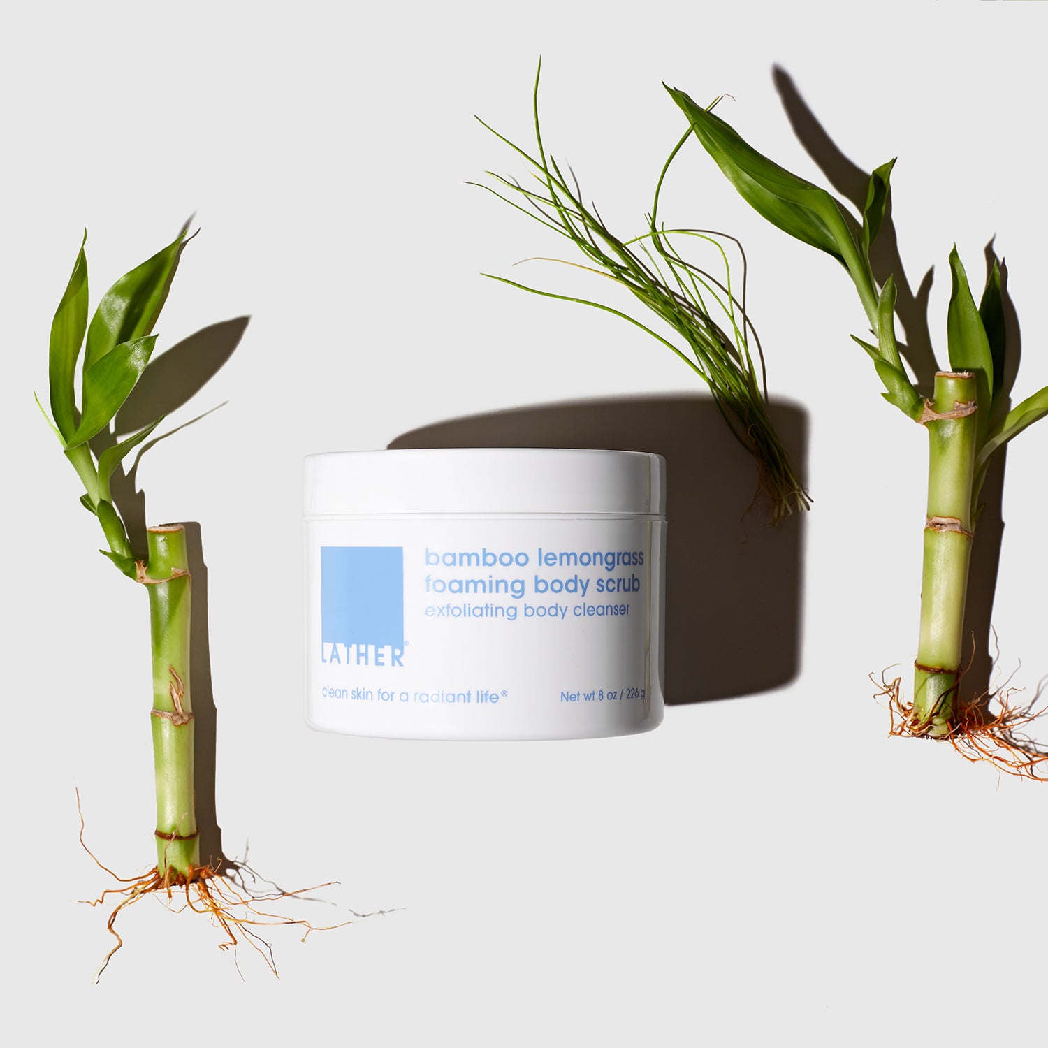 Bamboo Lemongrass Foaming Body Scrub product jar next to stalks of bamboo.